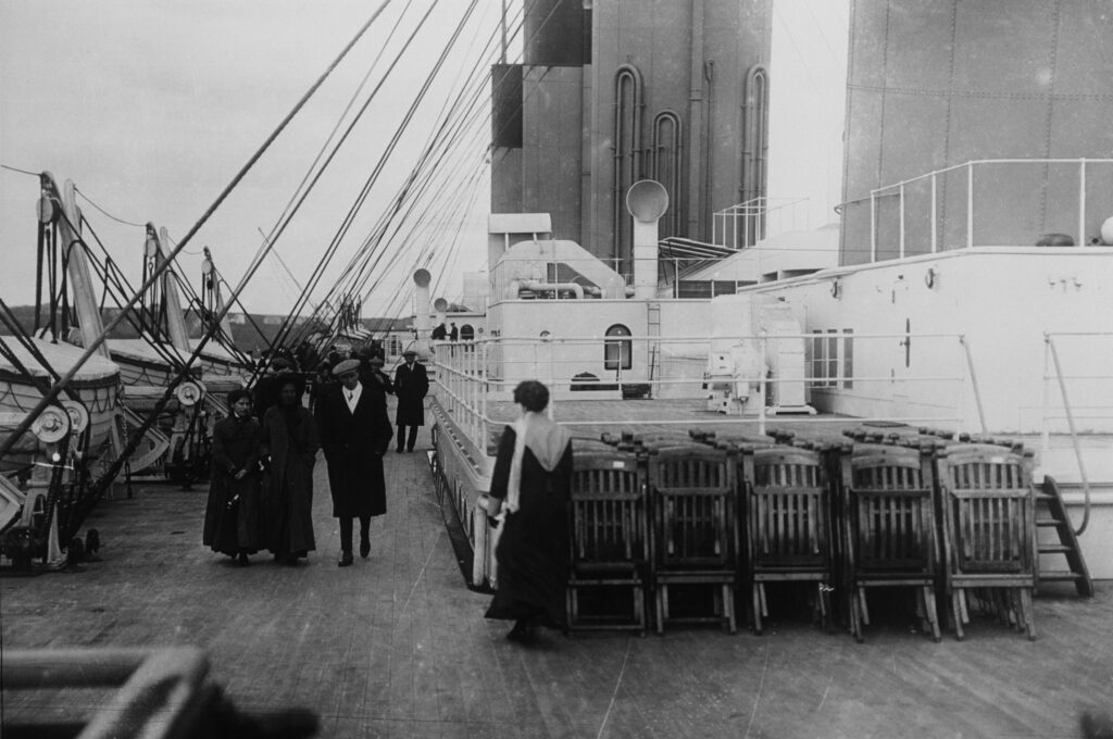 ca. 1912 --- Passengers stroll past neatly arranged deck chairs on the deck of the . The struck and iceberg and sank on her maiden voyage on April 14-15, 1912. --- Image by © Ralph White/CORBIS